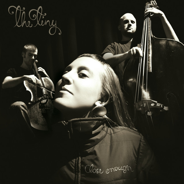 Album cover for The Tiny - Close Enough. In black and white, a woman looks toward the camera with her head angled to the upper left. A cellist and bassist stand behind her.